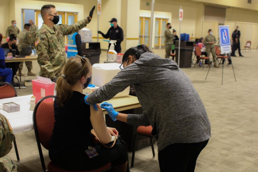 A woman receives a COVID-19 Vaccine while armed guards aid with distribution on Jan. 27, 2021.