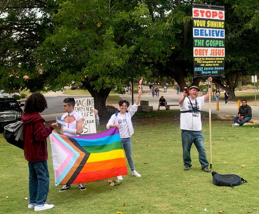 Students holding a pride flag counter protest next to a religious protestor holding a controversial sign on Oct. 17, 2022. 