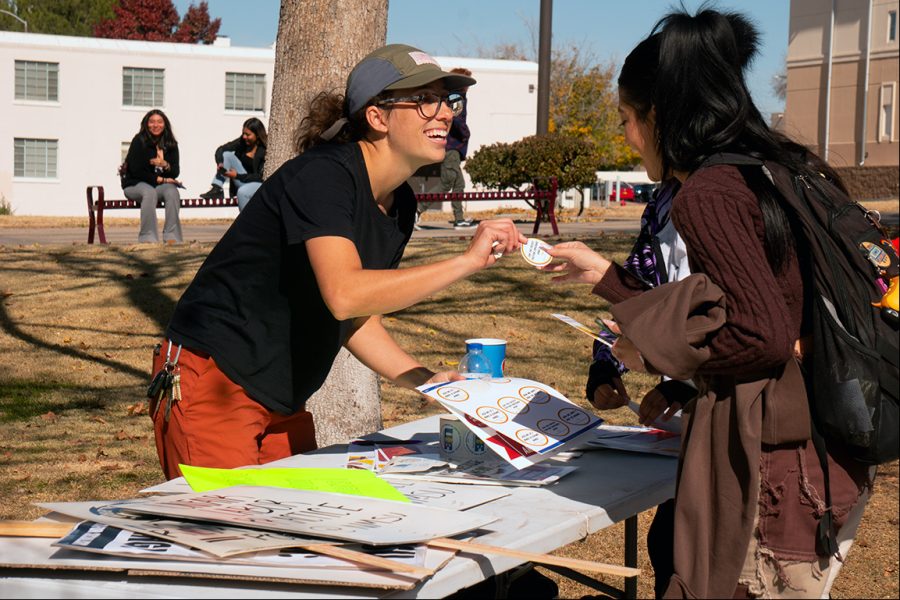 NMSU graduate student hands a sticker to a student during Thursdays protest outside Corbett Center on Dec. 1, 2022.