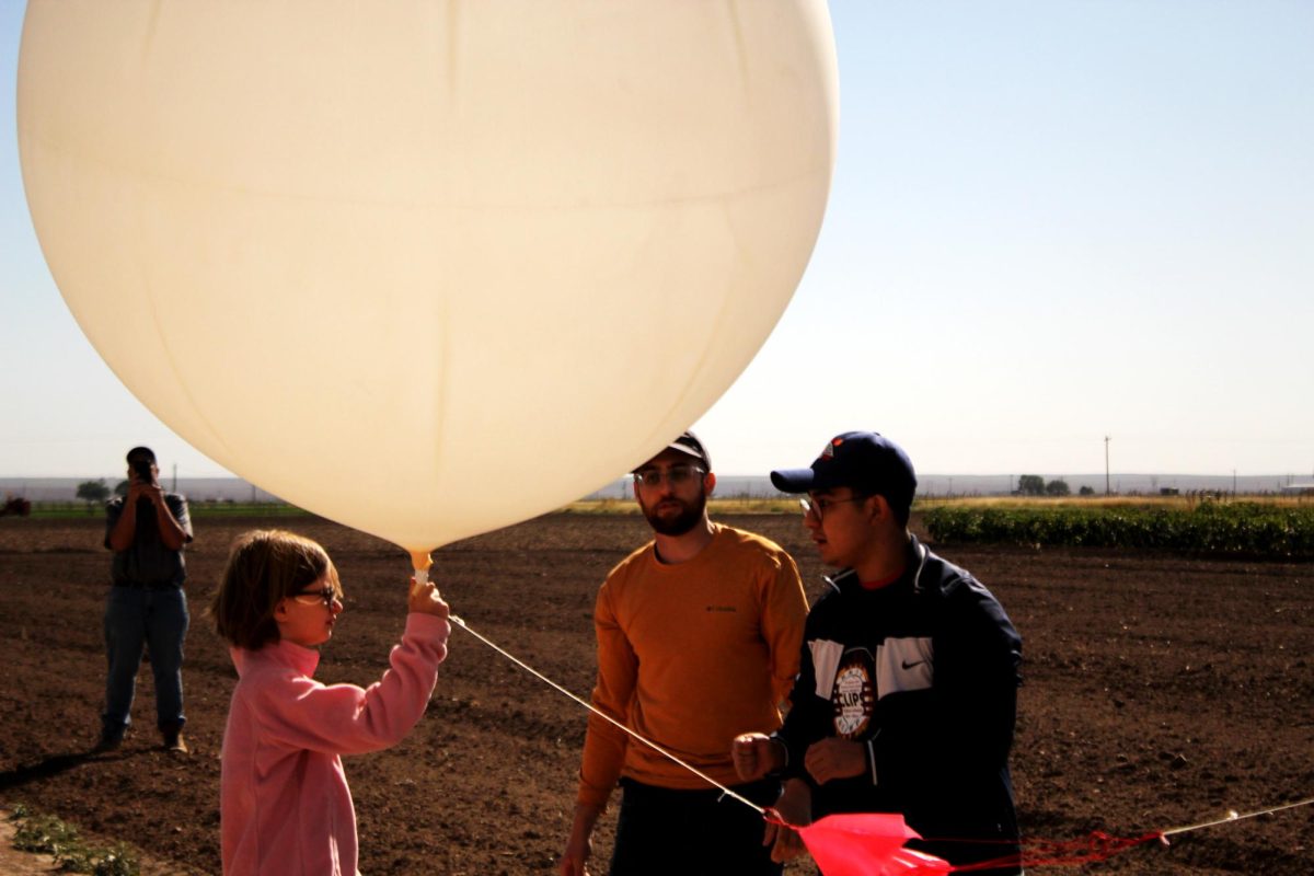 Students+Marco+Martinez+and+Shayan+Abotalebi+lend+a+helping+hand+to+a+young+girl+as+she+releases+a+weather+balloon+into+the+sky+on+Oct.+14%2C+2023.