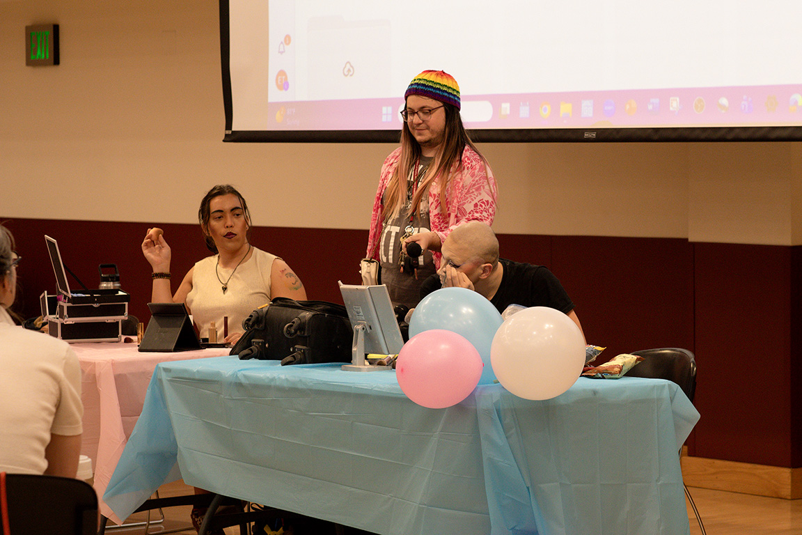 G.G. Bussy and Khaotica demonstrate how to apply drag makeup as LGBTQ+ Program Director Lore Falls holds the microphone. March 31, 2026. 

