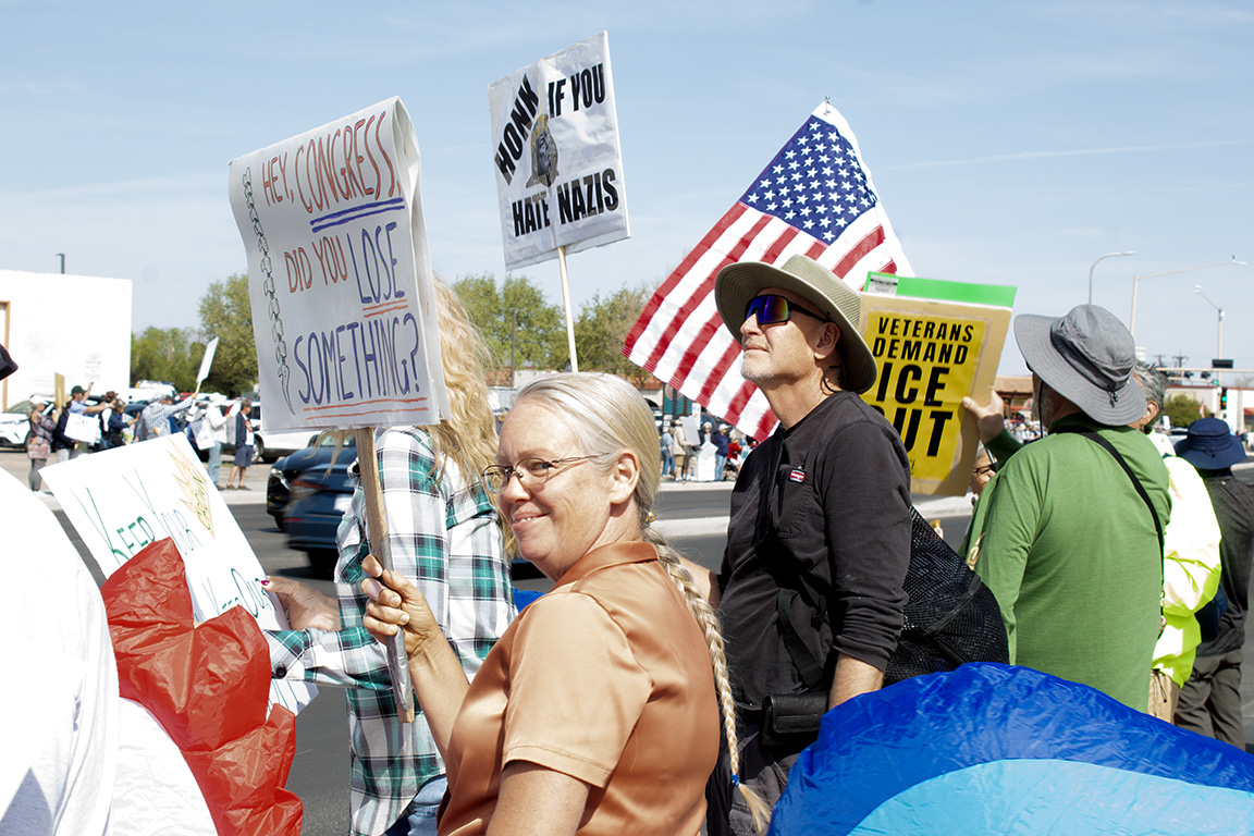 A protester smiles at the camera holding a sign which reads "Hey Congress, did you lose something?" picturing a set of vertebrae forming a spine. March 28, 2026.
