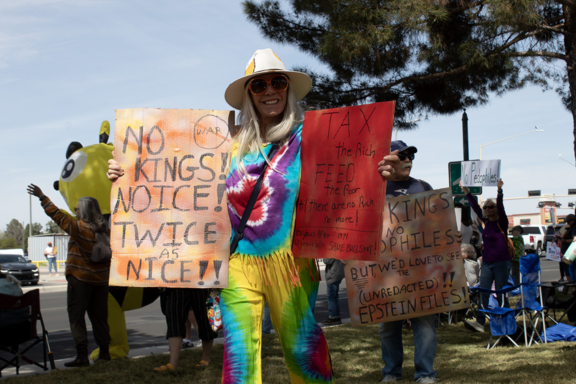 A protester in tie-dye holds signs that read "No Kings! No ICE! Twice as nice!!" and "Tax the rich feed the poor til there are no rich no more! Ten years after- 1971 55 years later, SAME BULLS**T!" March 28, 2026.