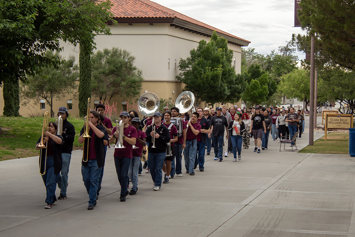 The Pride of New Mexico marching band leads the seniors past Clara Belle Williams Hall on April 30, 2026.